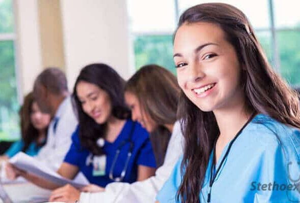 Group of healthcare professionals seated at a table, focused on paperwork and discussions. A person in the foreground smiles at the camera.
