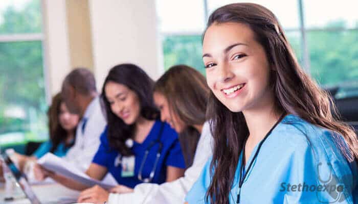 Group of healthcare professionals seated at a table, focused on paperwork and discussions. A person in the foreground smiles at the camera.
