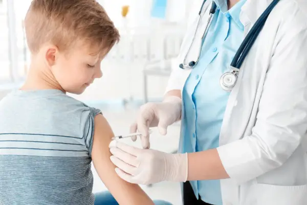 A healthcare professional administers a vaccine to a young boy's arm in a clinical setting.